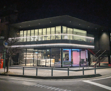 青空の下に建つ「KYUKARU SALON（旧軽サロン）」の外観。モダンな黒い建物が目を引き、隣には「Ferrari」の大きなロゴが描かれた別の建物が並んでいます。街角に位置し、広いガラス窓と赤い階段が特徴的です。